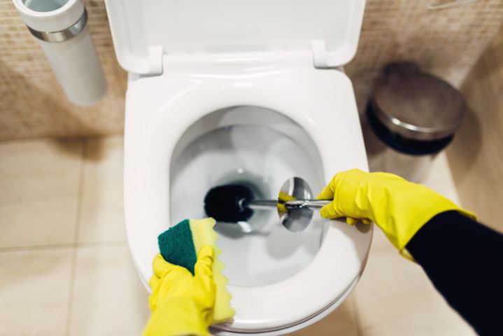 Housemaid in gloves cleans the toilet with brush